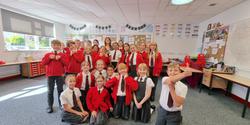 Image at a theatre workshop, shows 20 school children smiling and waving at the camera