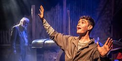 Production shot of Farmboy in the Garrick Studio, a young man sits on a chair at the front of the stage with his arms in the air and an old tractor in the background